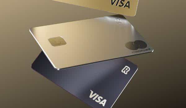 Cartão Revolut Metal na cor dourada e com bandeira Mastercard à frente na imagem e dois modelos de outras cores e bandeira Visa na parte de trás.