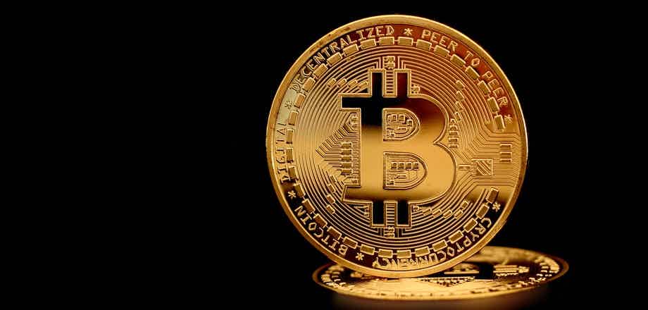 Imagem ilustrativa de uma moeda de Bitcoin na cor dourada com fundo preto