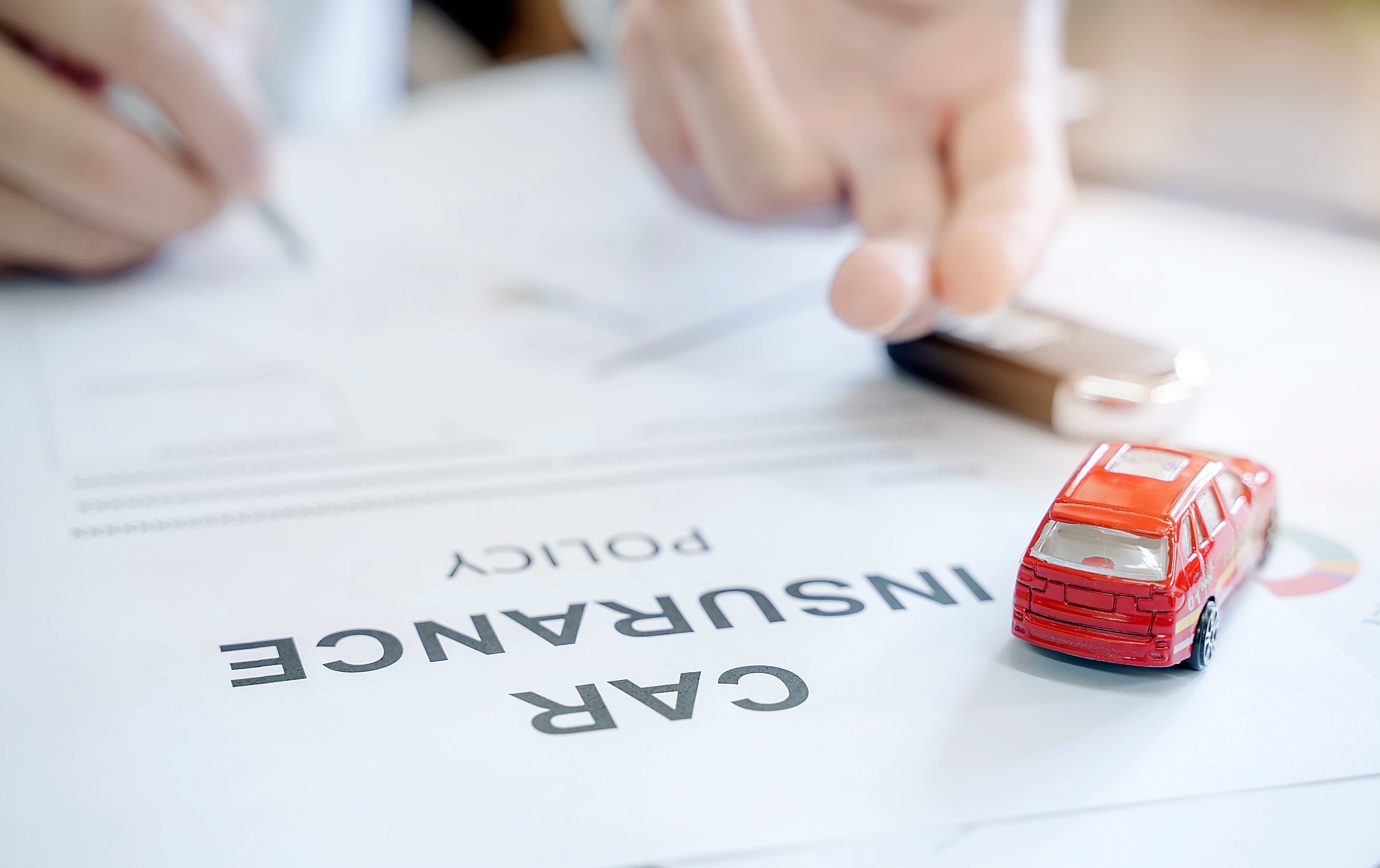 zoom of a paper with the words CAR INSURANCE and a car miniature on the side