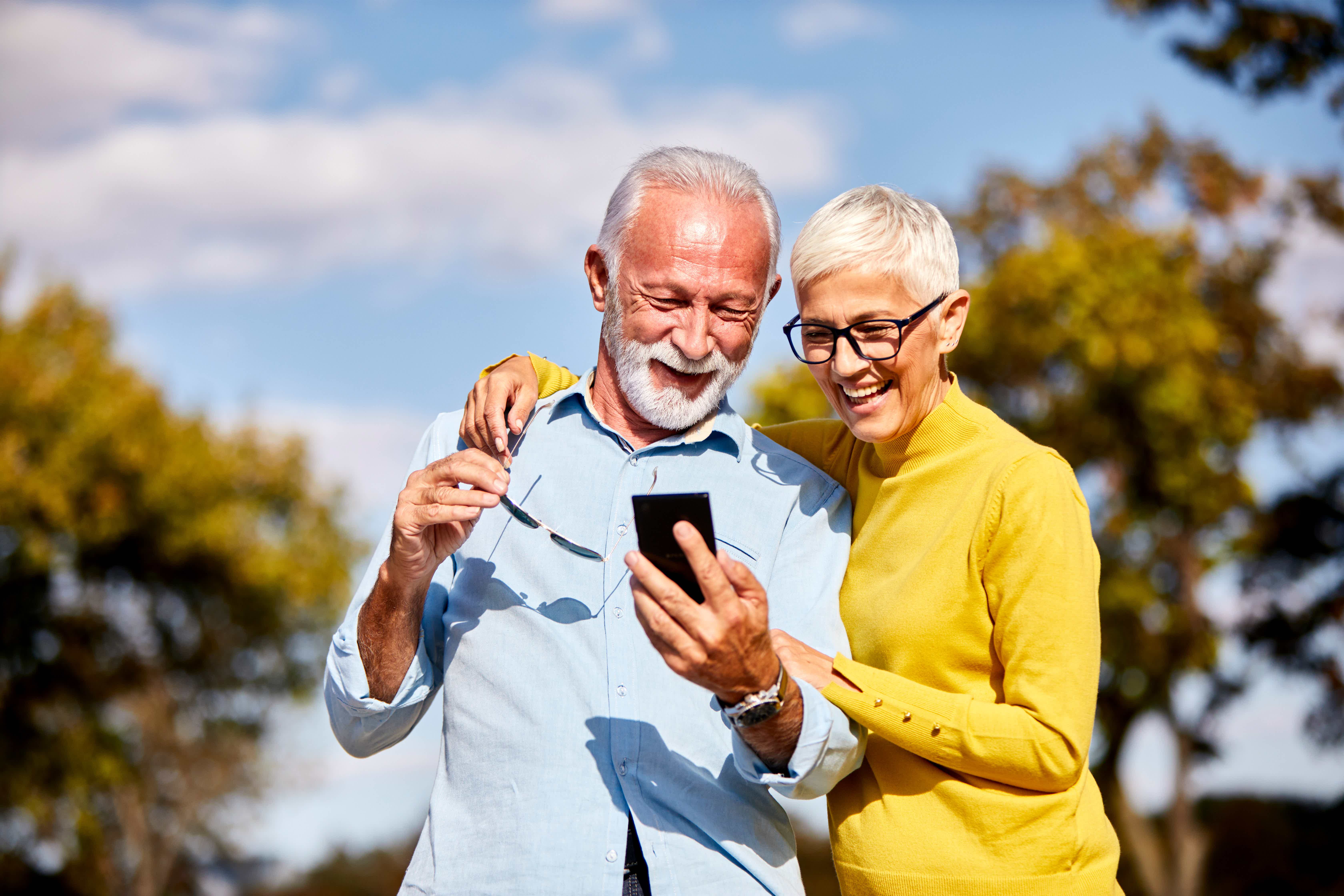 Pareja de ancianos mirando un teléfono móvil, simbolizando las aplicaciones de citas para la tercera edad.