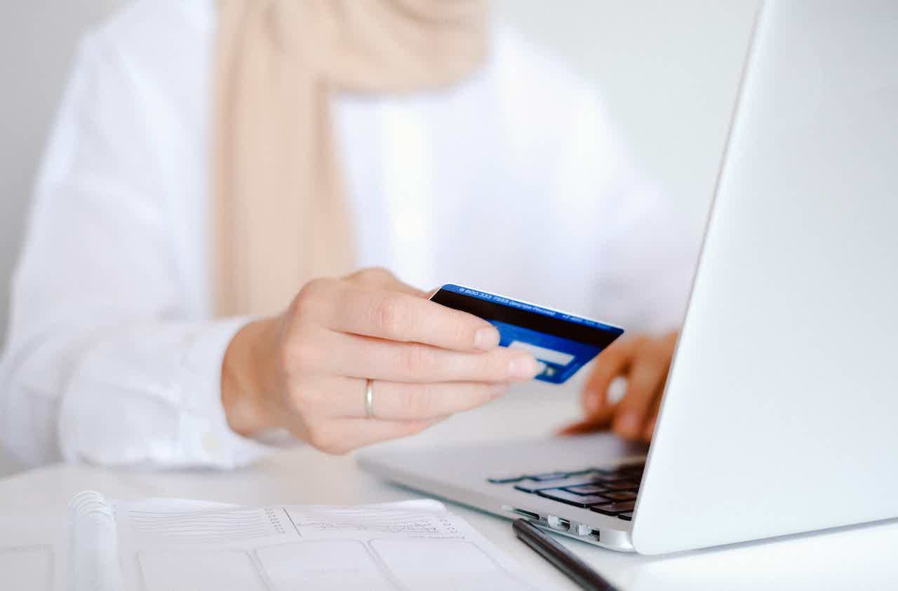 Mulher segurando cartão de crédito azul enquanto digita algo em seu notebook