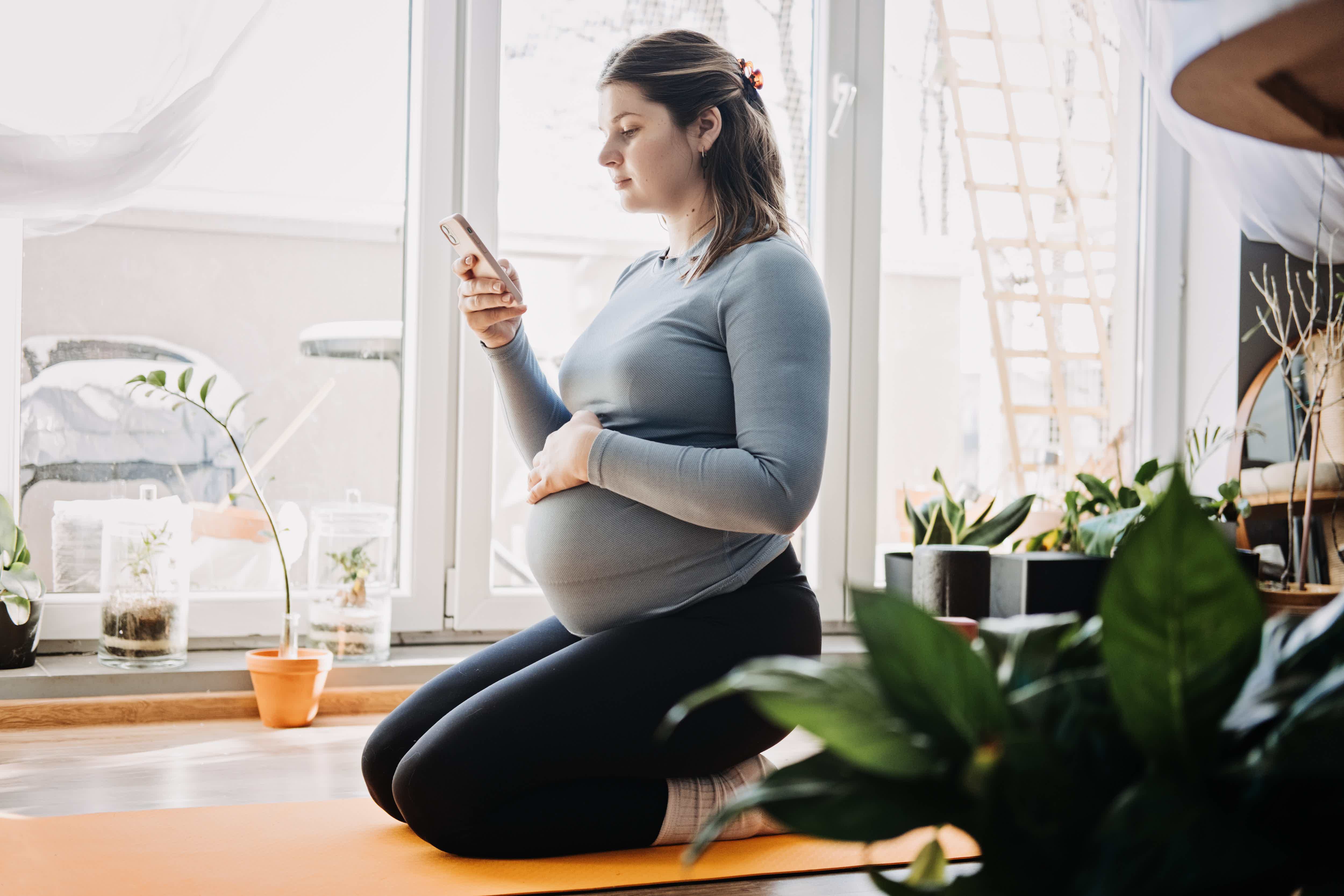 Mulher grávida sentada no chão olhando celular