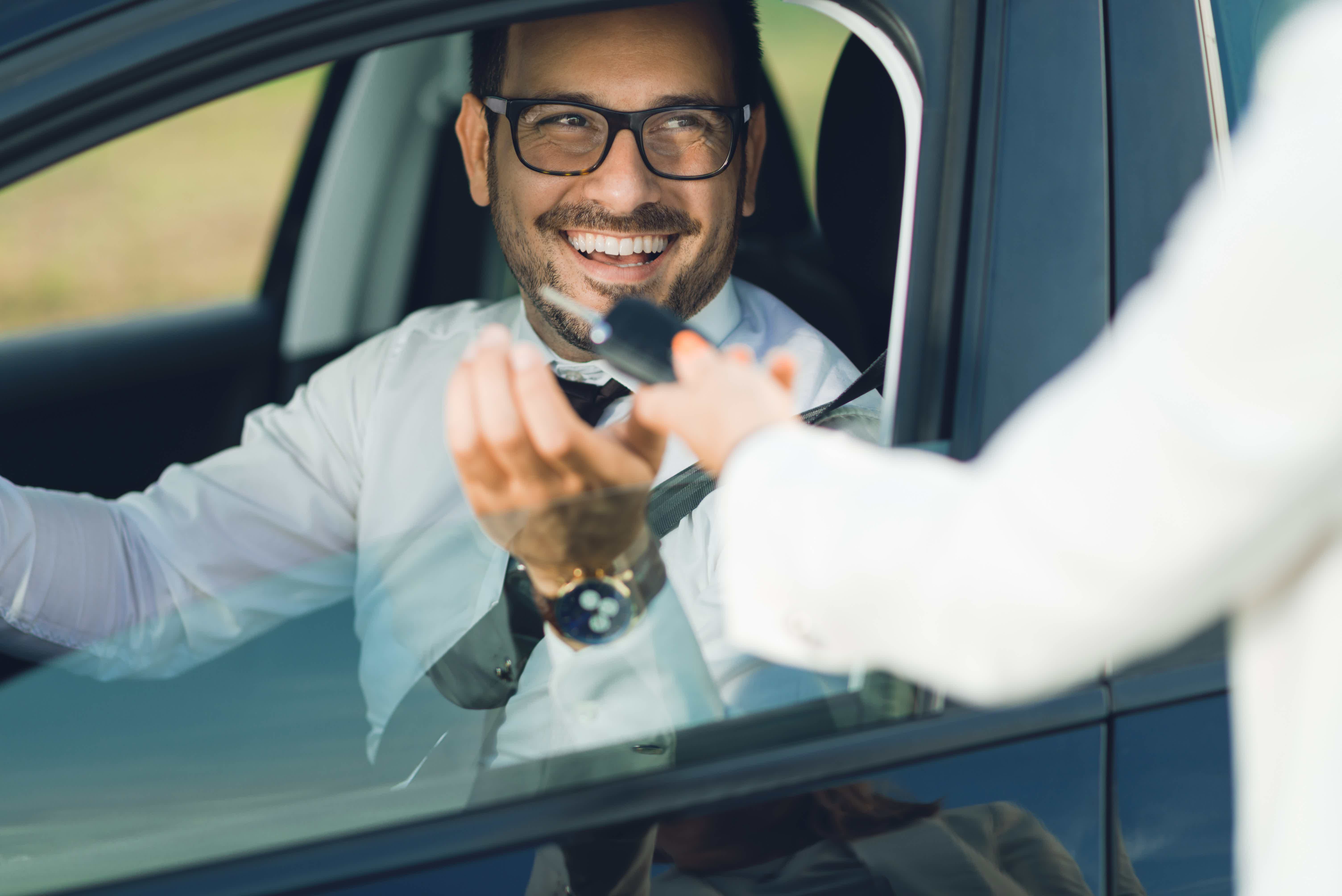 Homem sorrindo recebendo chaves de carro, sentado no banco do motorista