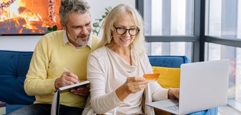 Homem e mulher de meia idade sentados observando um cartão de crédito que está na mão da mulher.