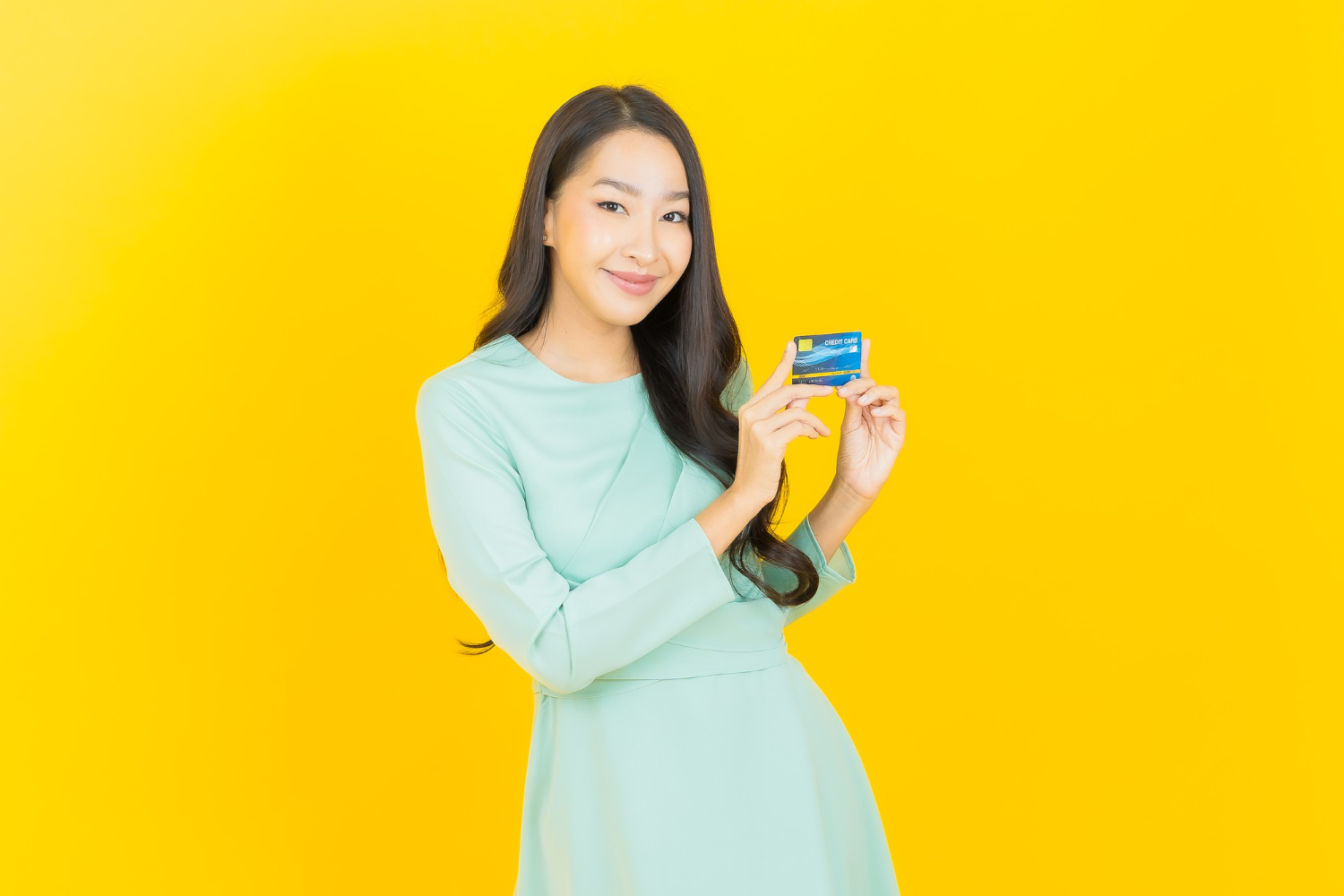 jovem asiática sorrindo com cartão de crédito em amarelo