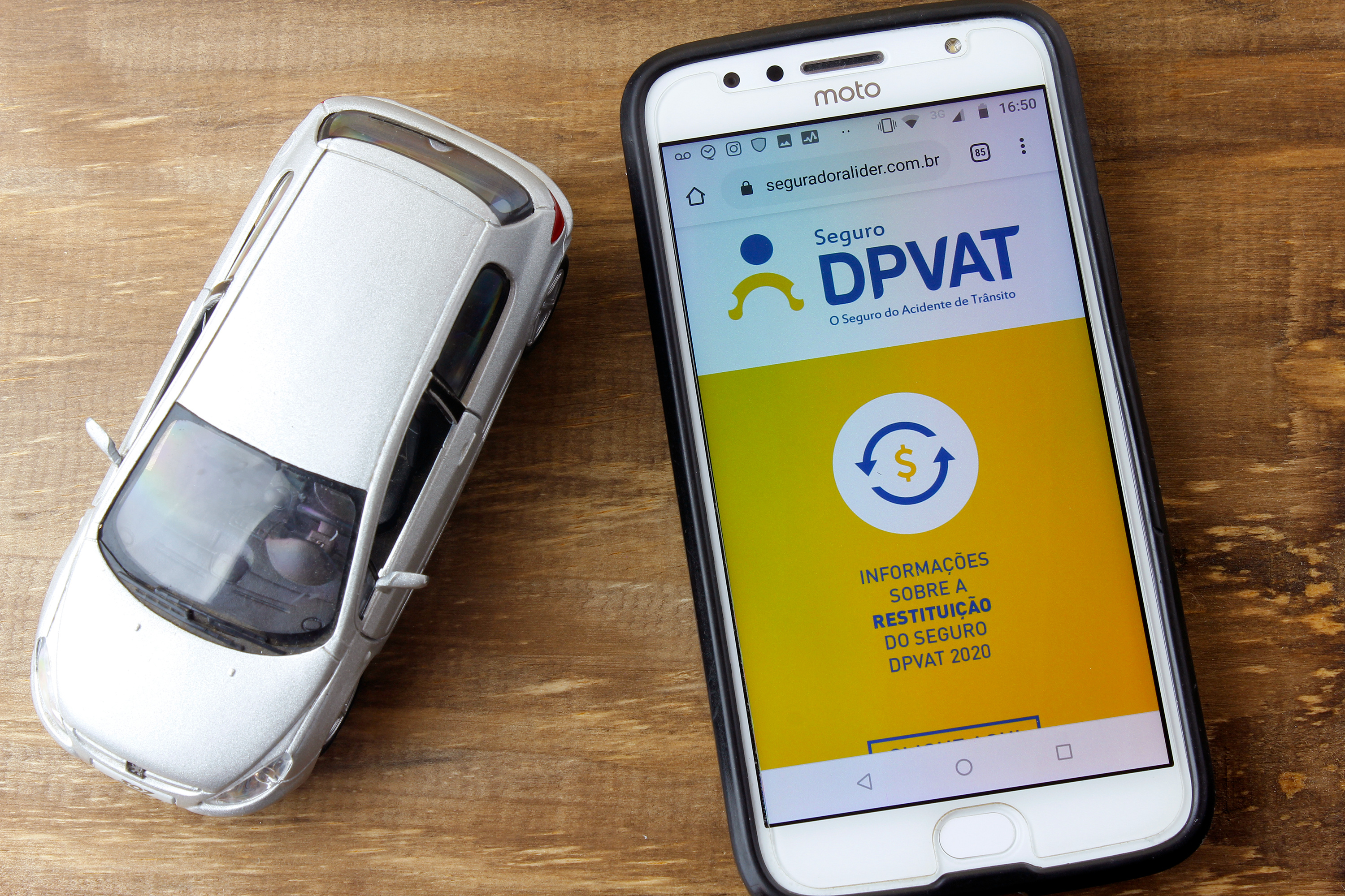 Celular com DPVAT aberto e miniatura de carro ao lado
