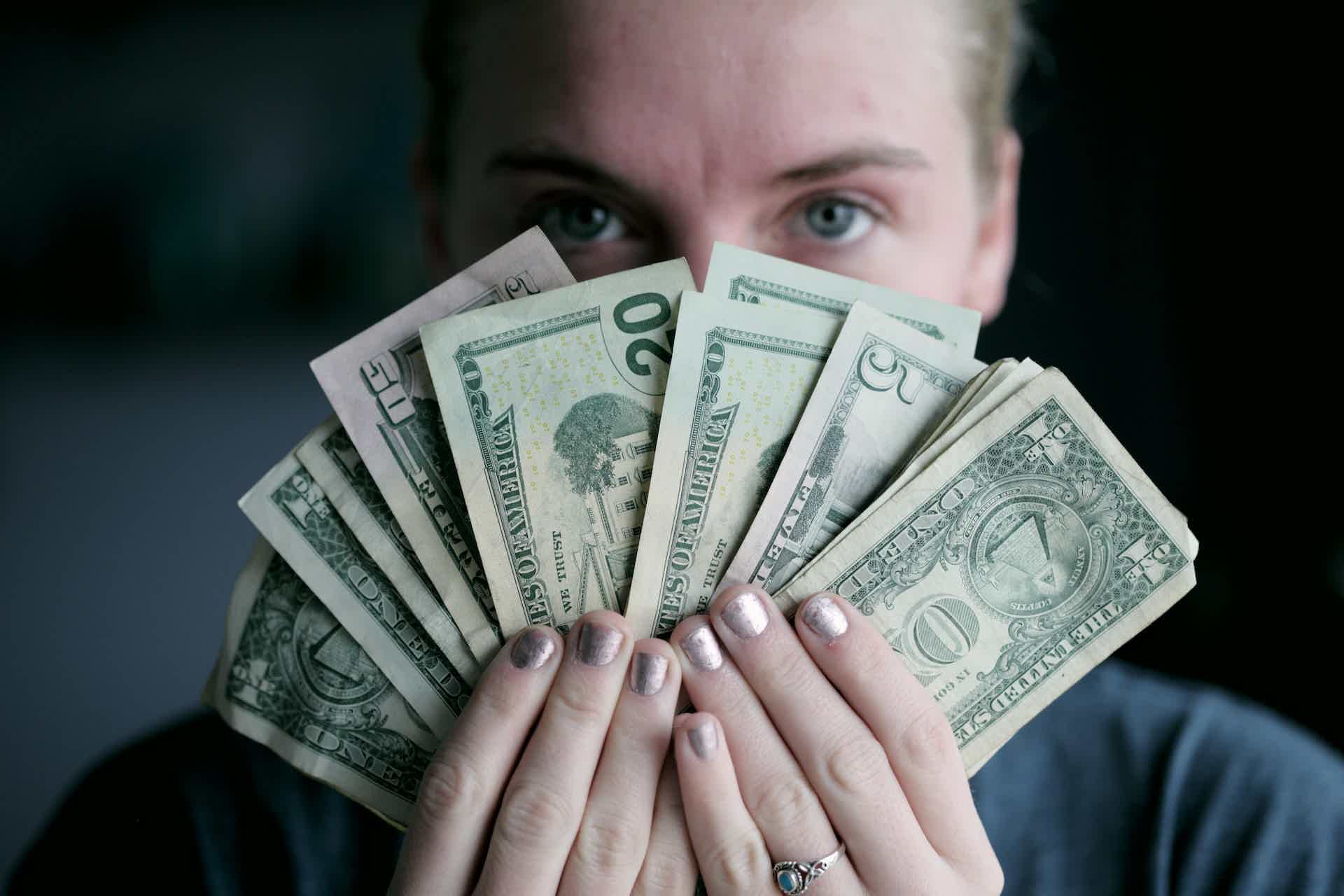 Mulher segurando várias notas de dinheiro em formato de leque em frente ao seu rosto