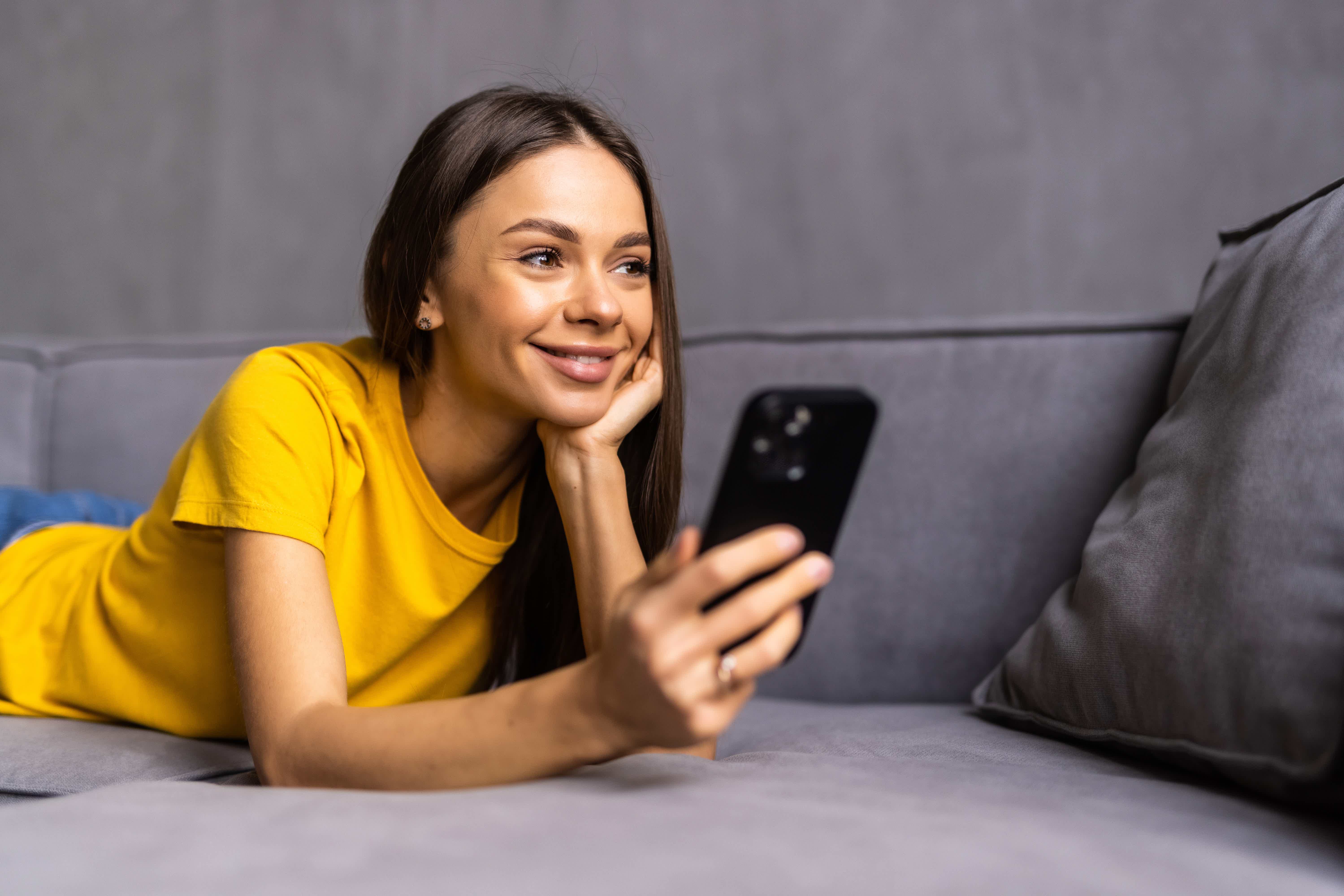 Mulher sorrindo usando celular e olhando tv