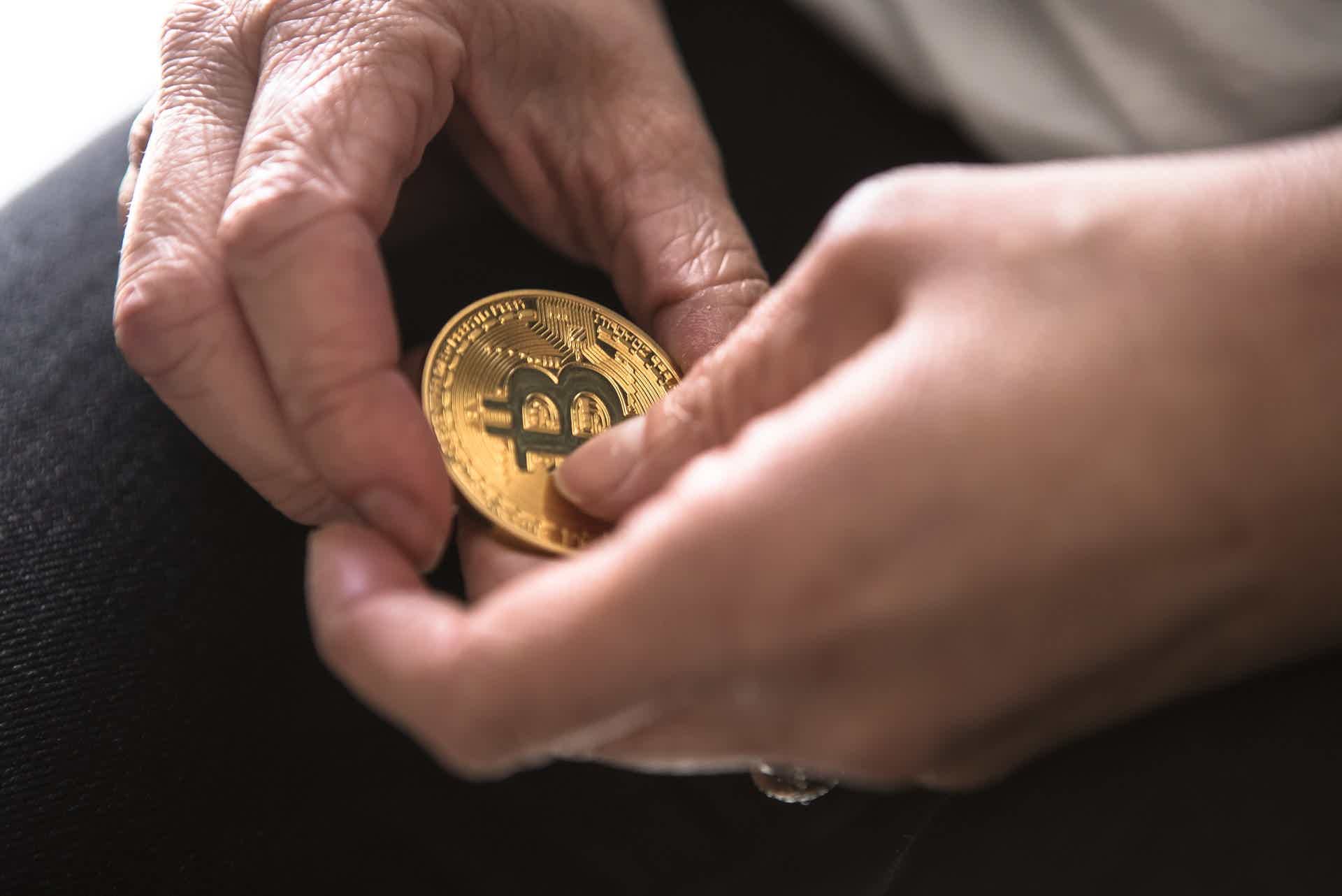 two hands holding a physical representation of a Bitcoin