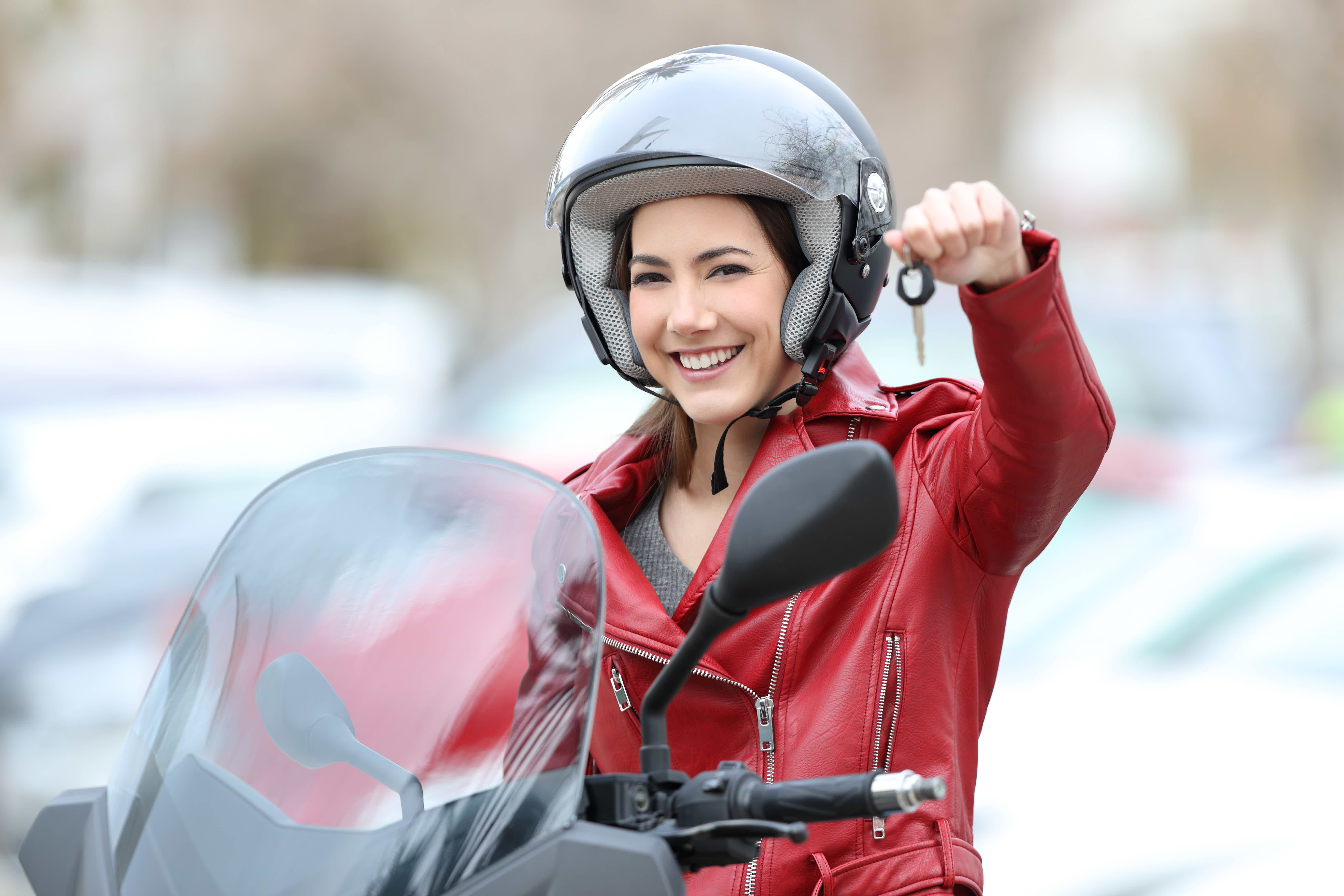 Mulher sorrindo sobre a moto apontando chave para câmera