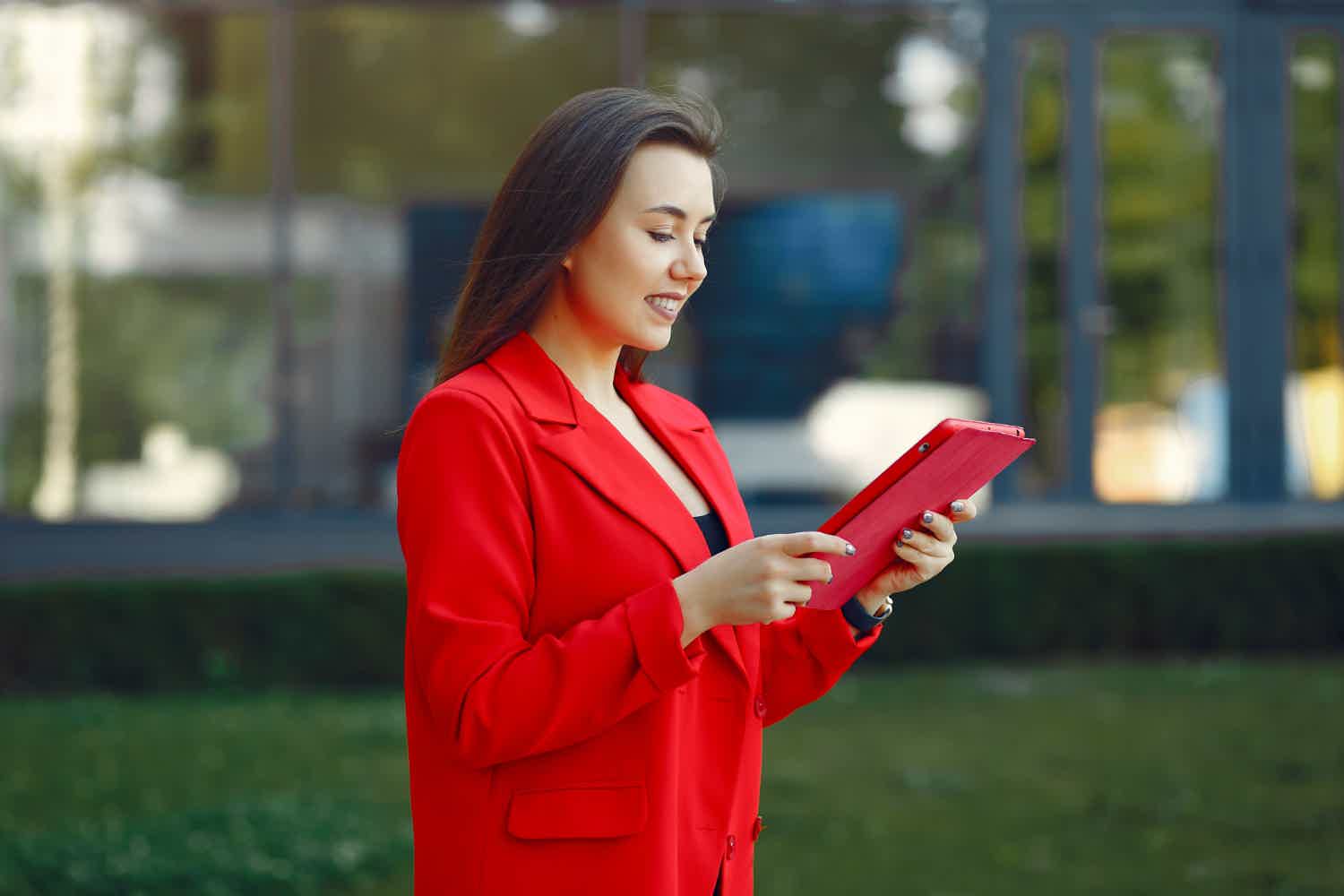 Mulher de blazer vermelho andando enquanto usa seu tablet