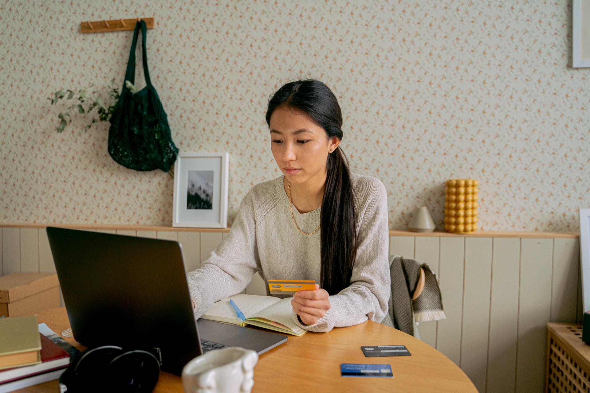 Mulher sentada com cartão de crédito na mão e notebook em uma mesa. Fonte: Pexels