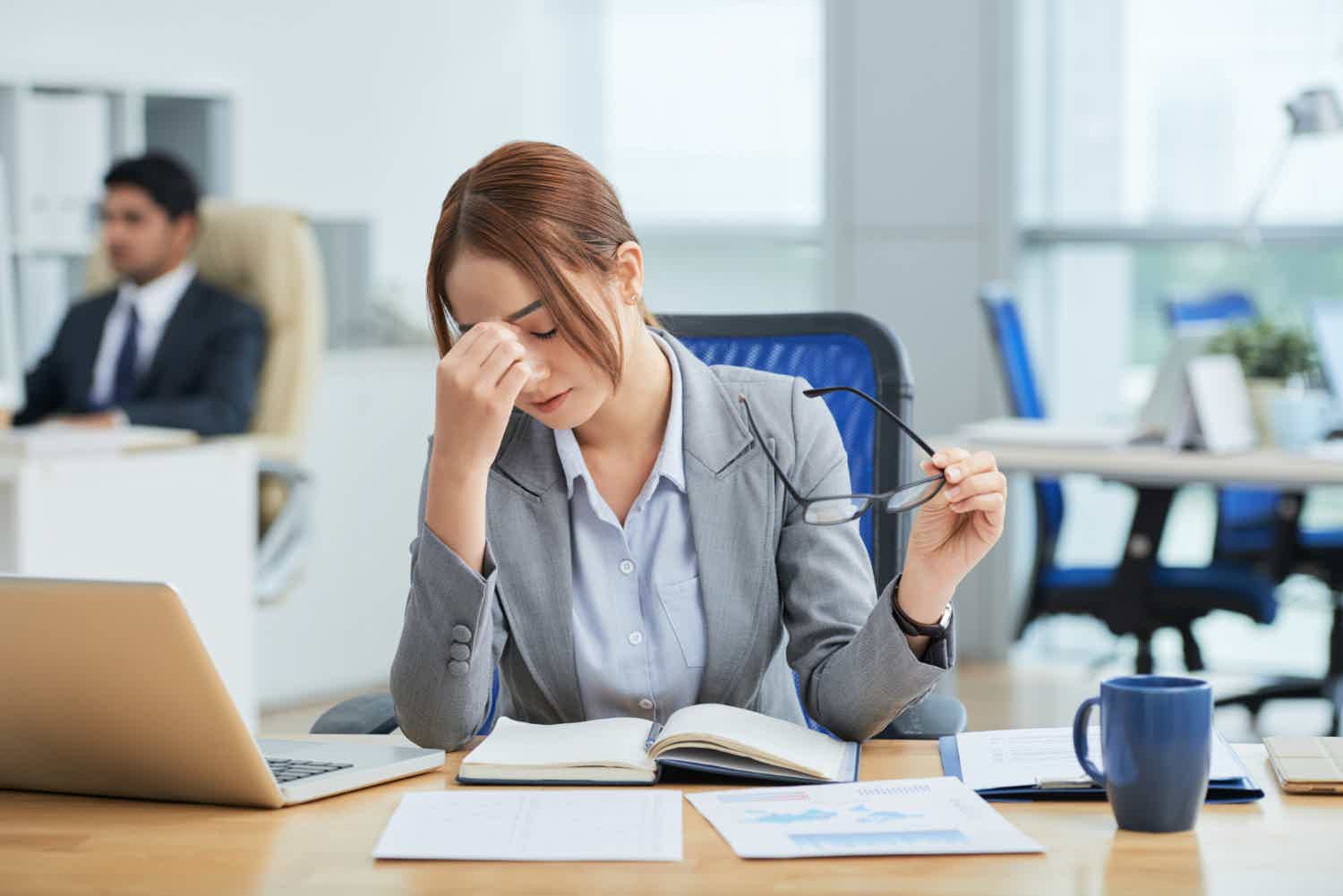 business woman sad head down holding glasses office desk