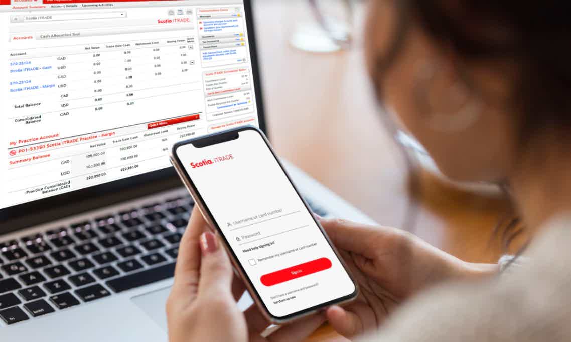 Pessoa segurando celular com aplicativo Scotia iTRADE e computador ao fundo no site Scotia iTRADE