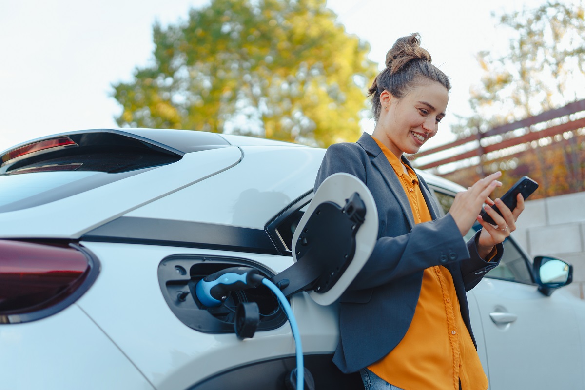 mulher de blusa laranja mexendo no celular enquanto espera o seu carro elétrico carregar
