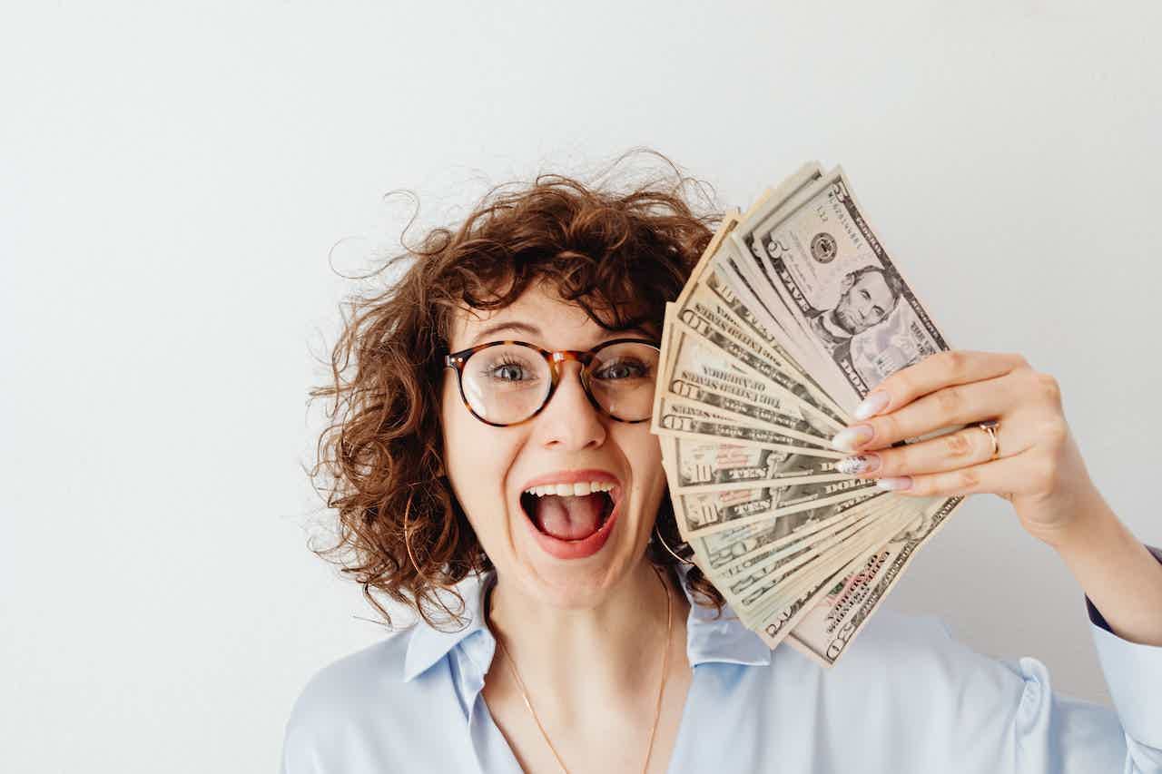Mulher sorrindo enquanto segura um leque de notas de dólares