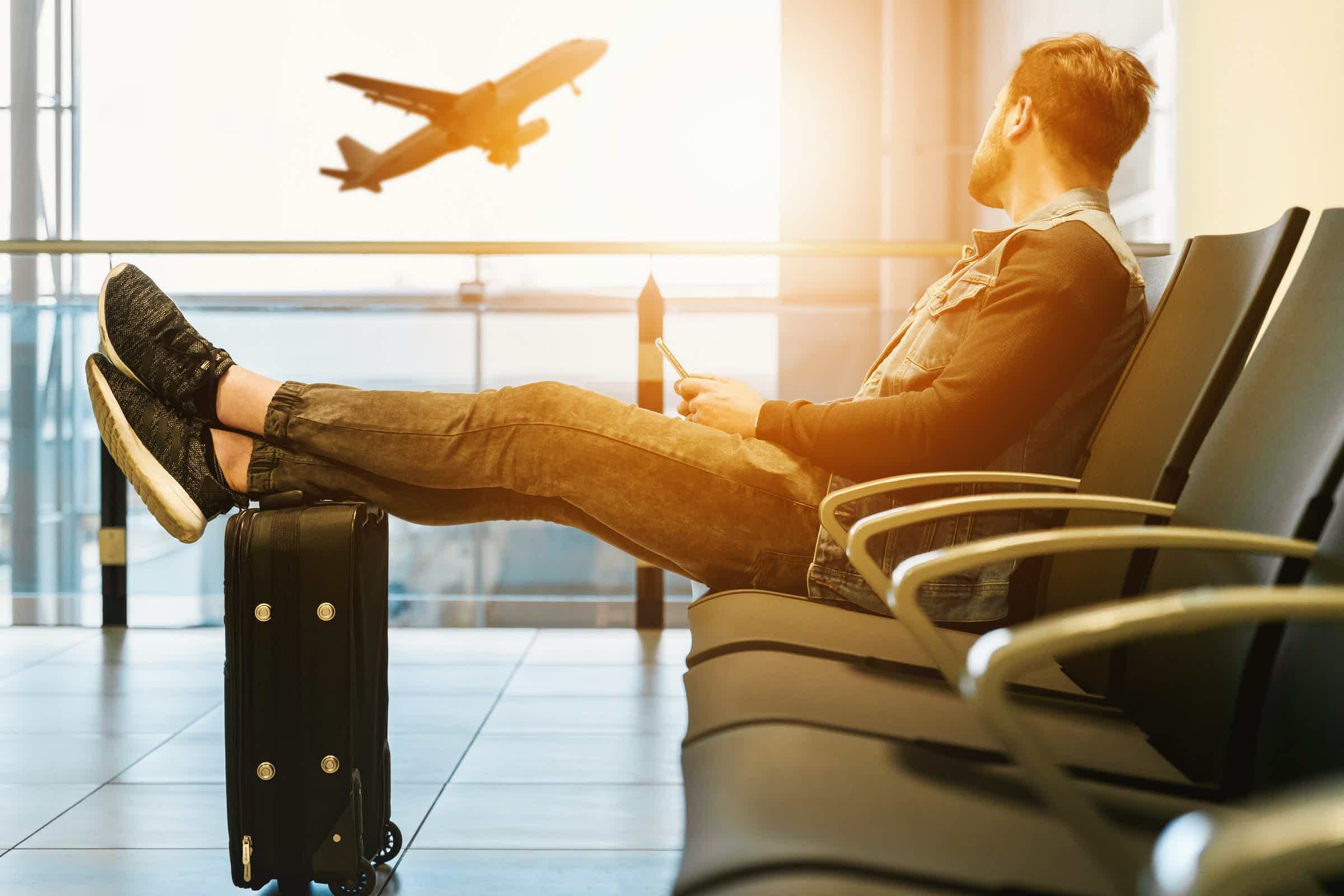 homem sentado em um aeroporto olhando para um avião decolar