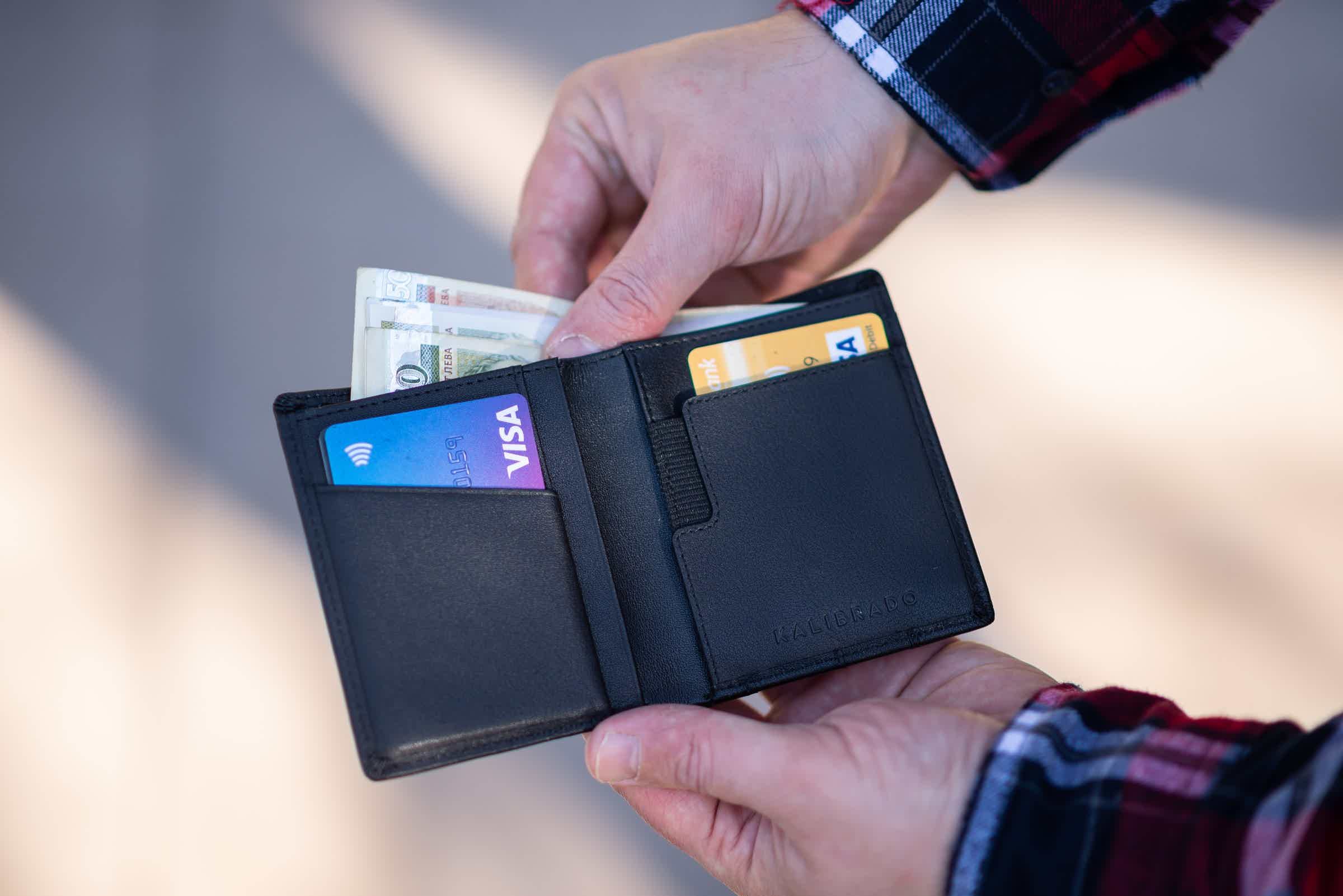 duas mãos segurando uma carteira com cartões de crédito e dinheiro