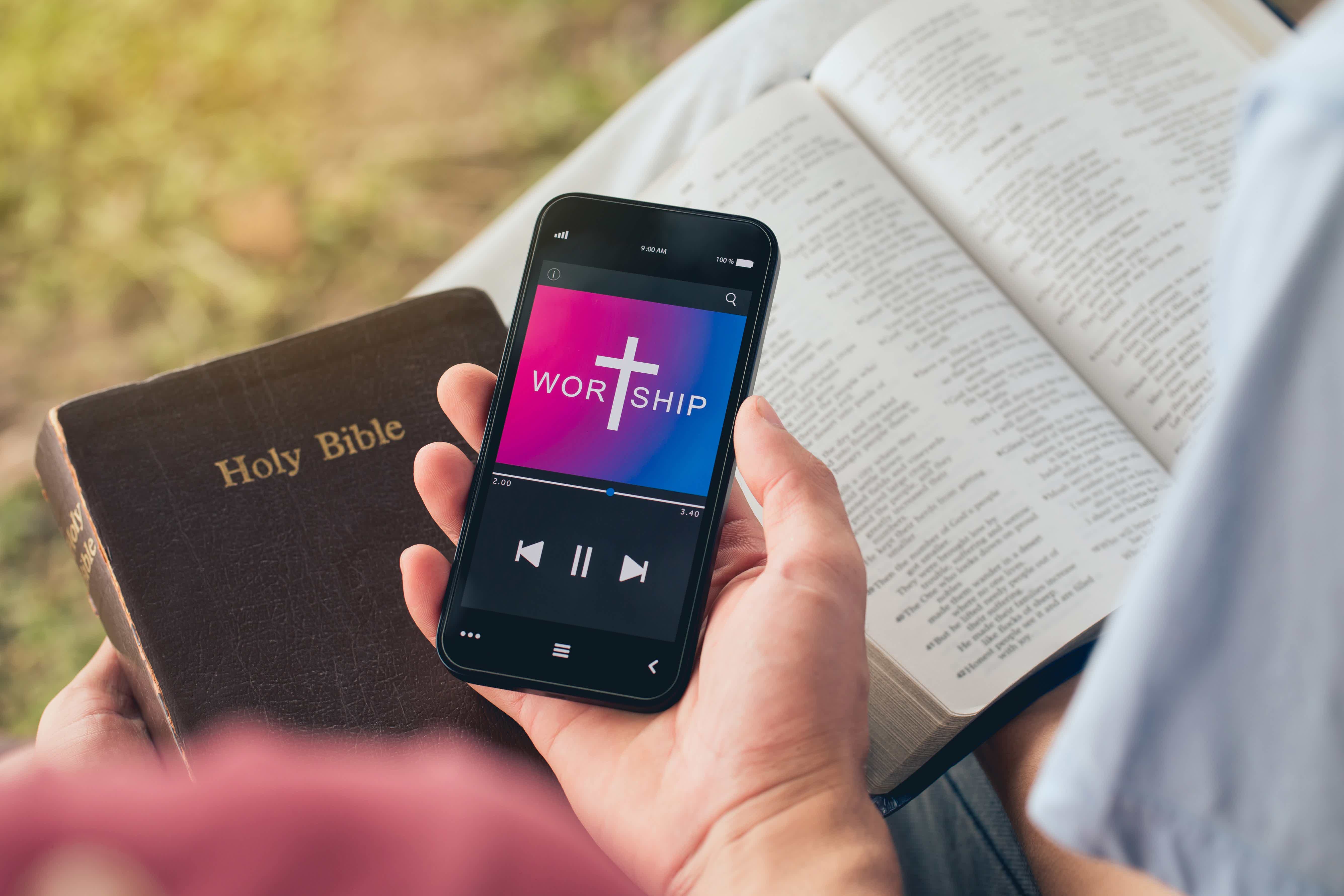 Pessoa com bíblias na mão e um aplicativo de música. 
