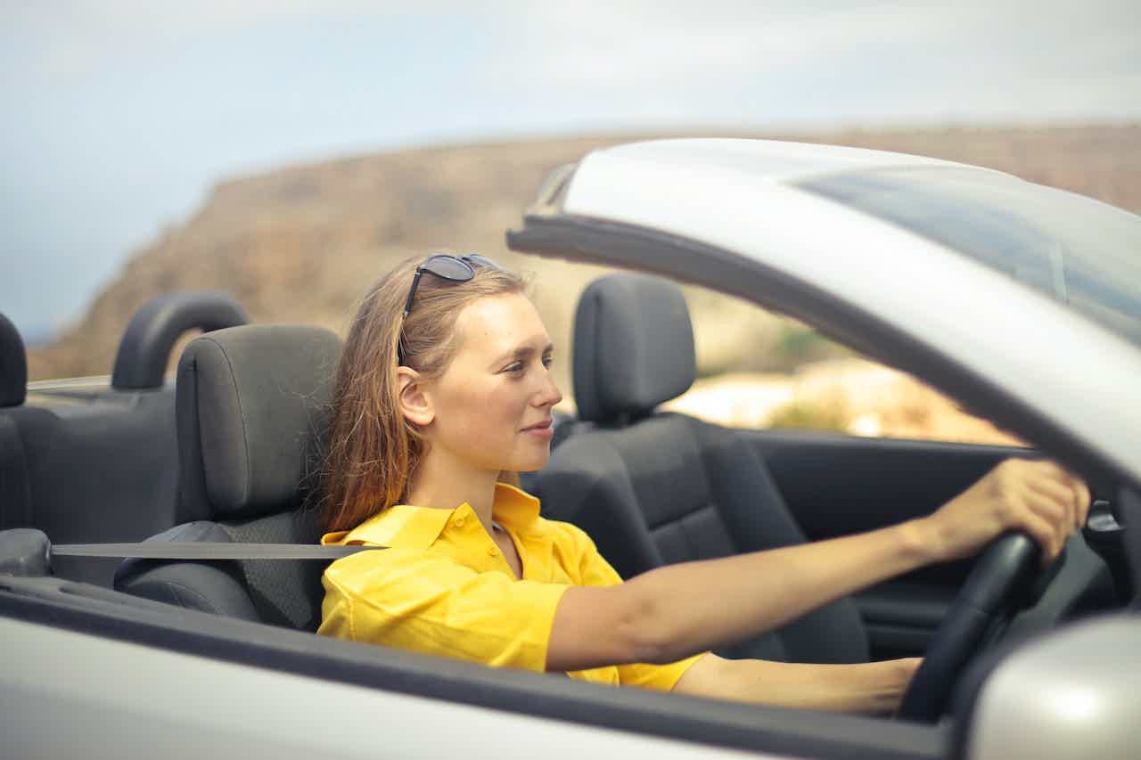 Mulher usando camiseta amarela dirigindo um carro conversível