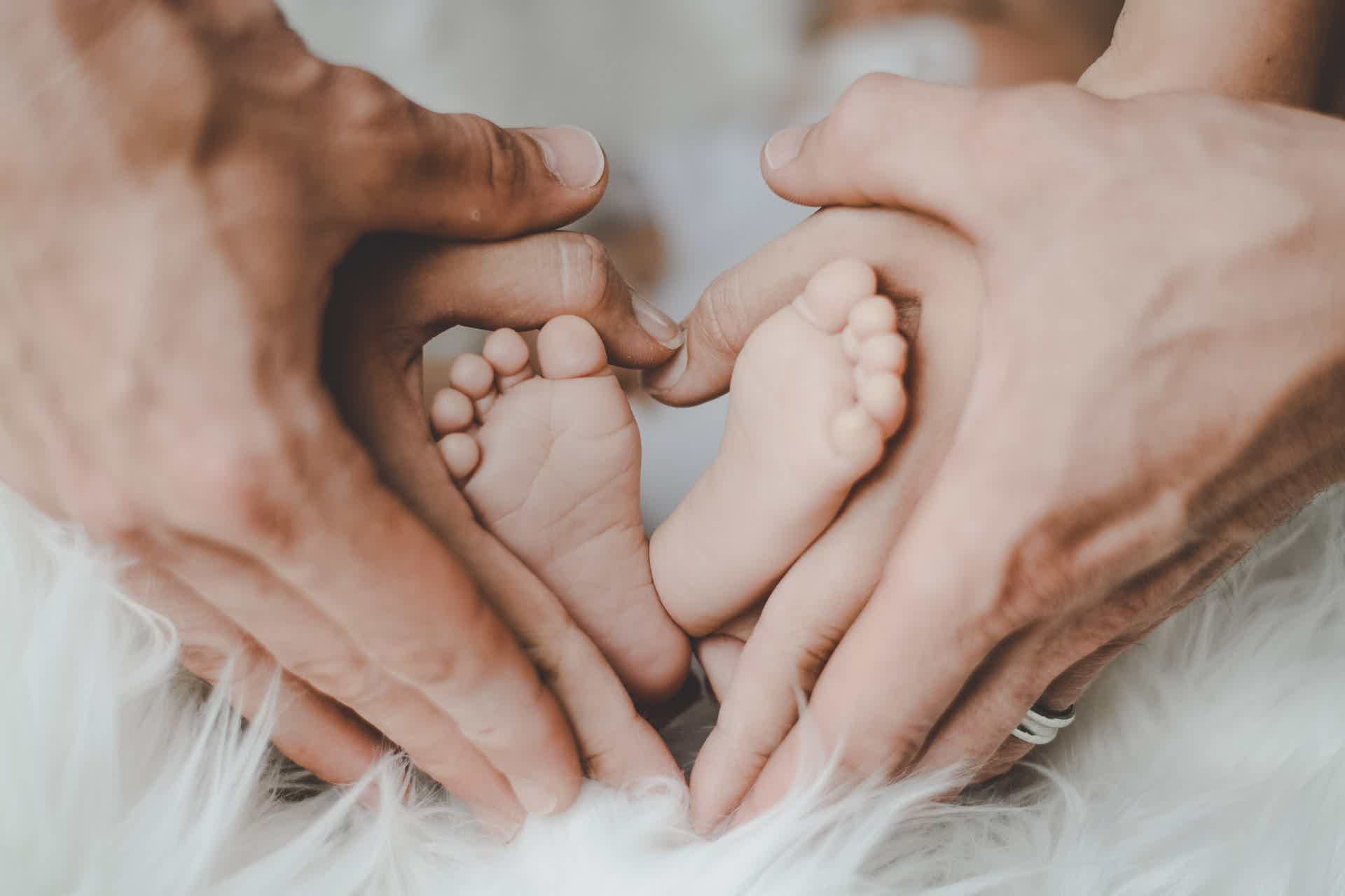 Pai e mãe fazendo coração com as mãos em volta do pé do filho. Fonte: Pexels