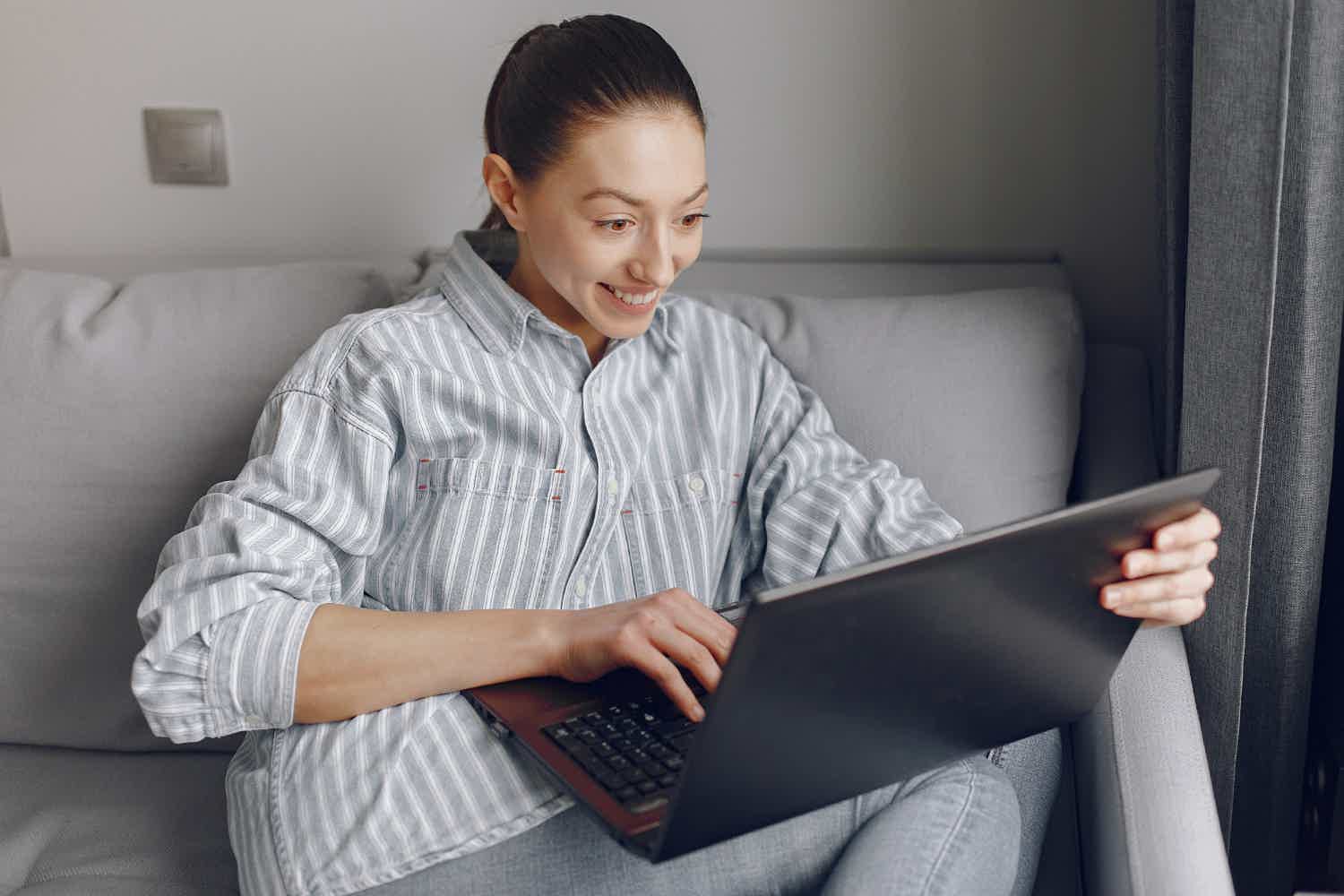 Mulher feliz usando camisa listrada enquanto usa seu notebook