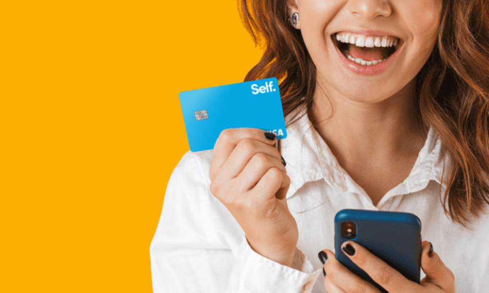 Mulher segurando cartão Self Visa Credit Builder e celular