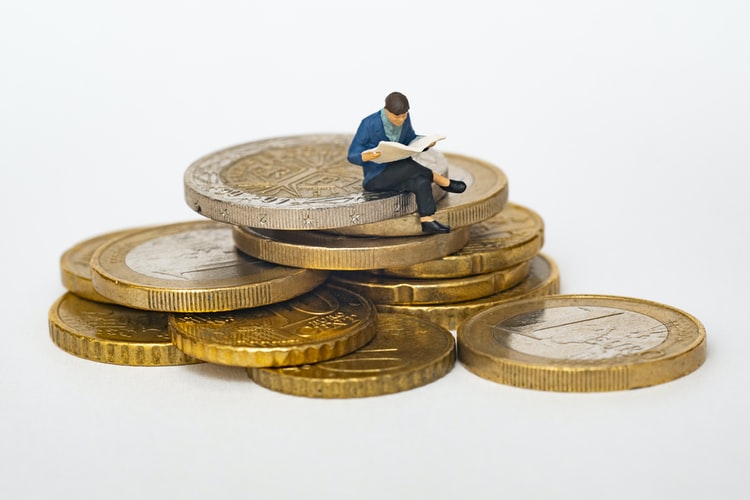 a pile of coins in a white background with a small man sitting over it