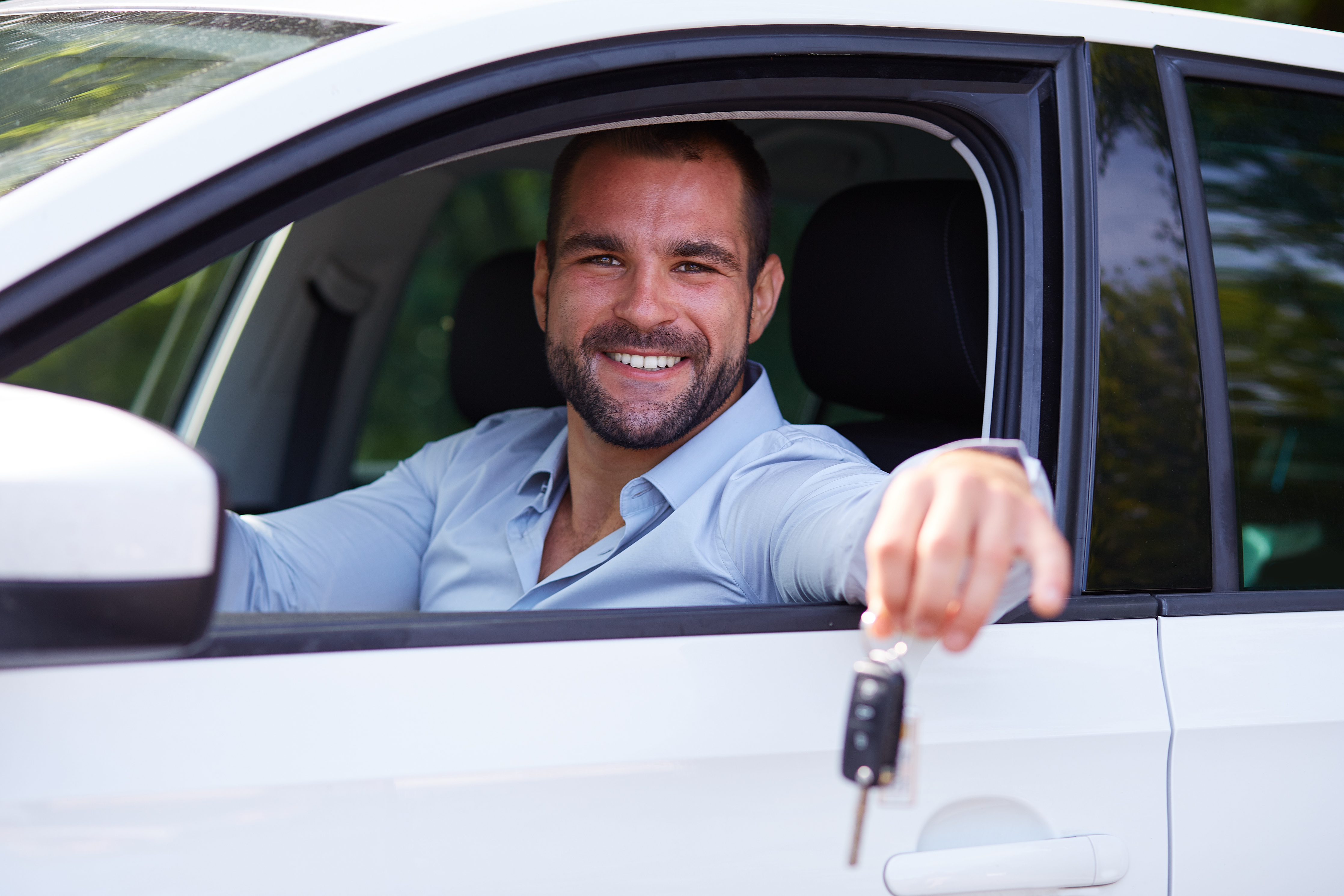 Homem sorrindo, segurando chaves para fora do carro