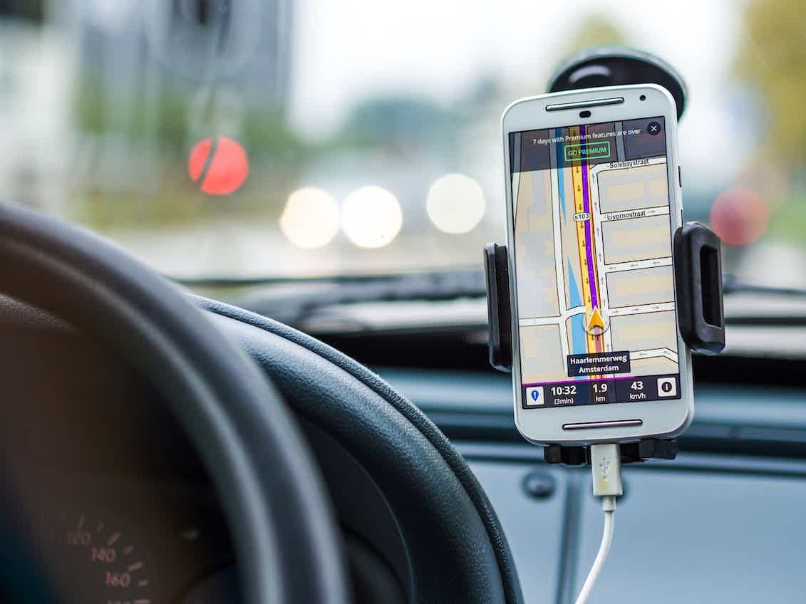 Celular branco dentro de um carro mostrando uma rota no GPS
