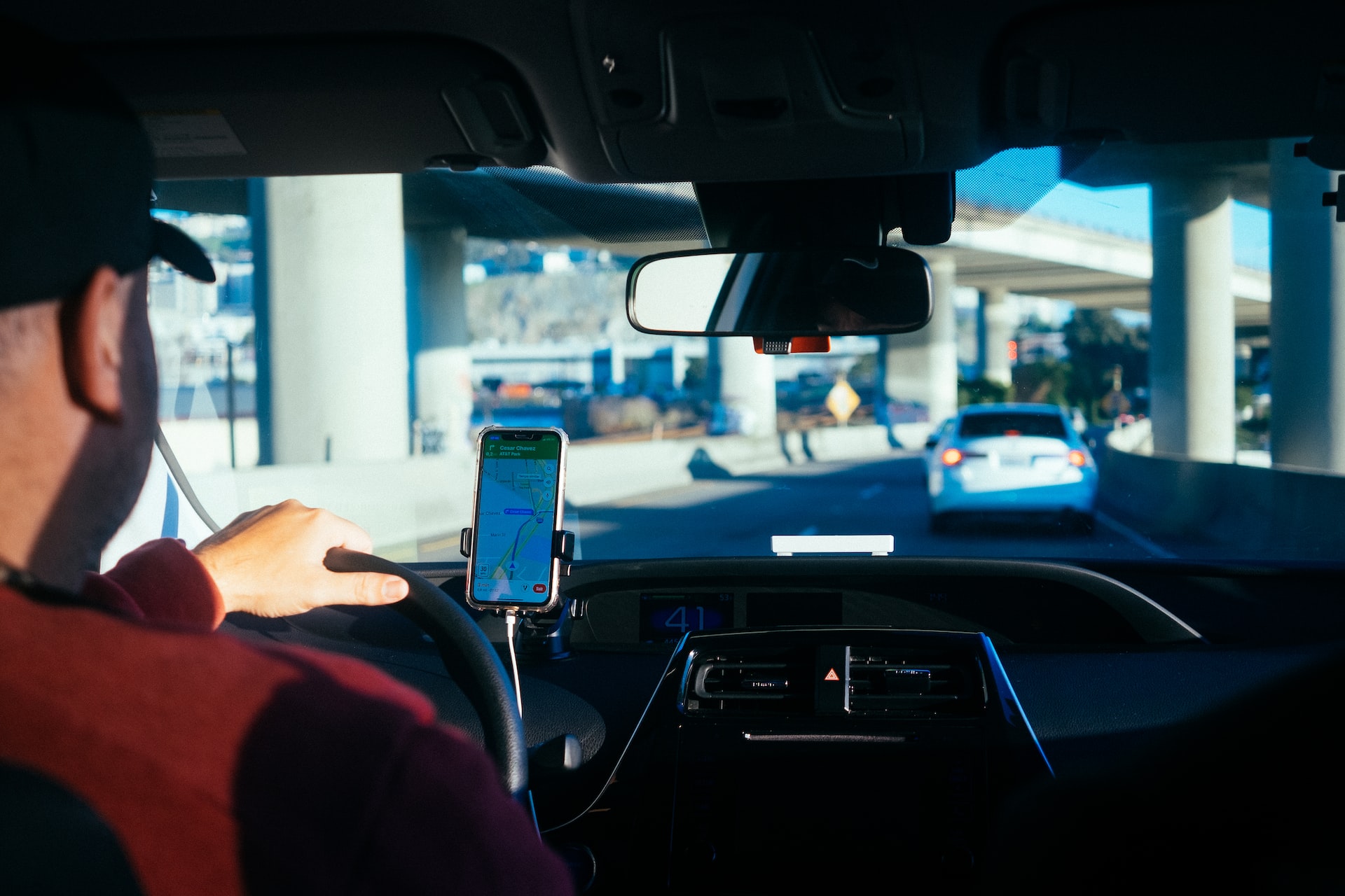 Motorista de aplicativo comas mãoes no volante e seu celular ao lado com a rota