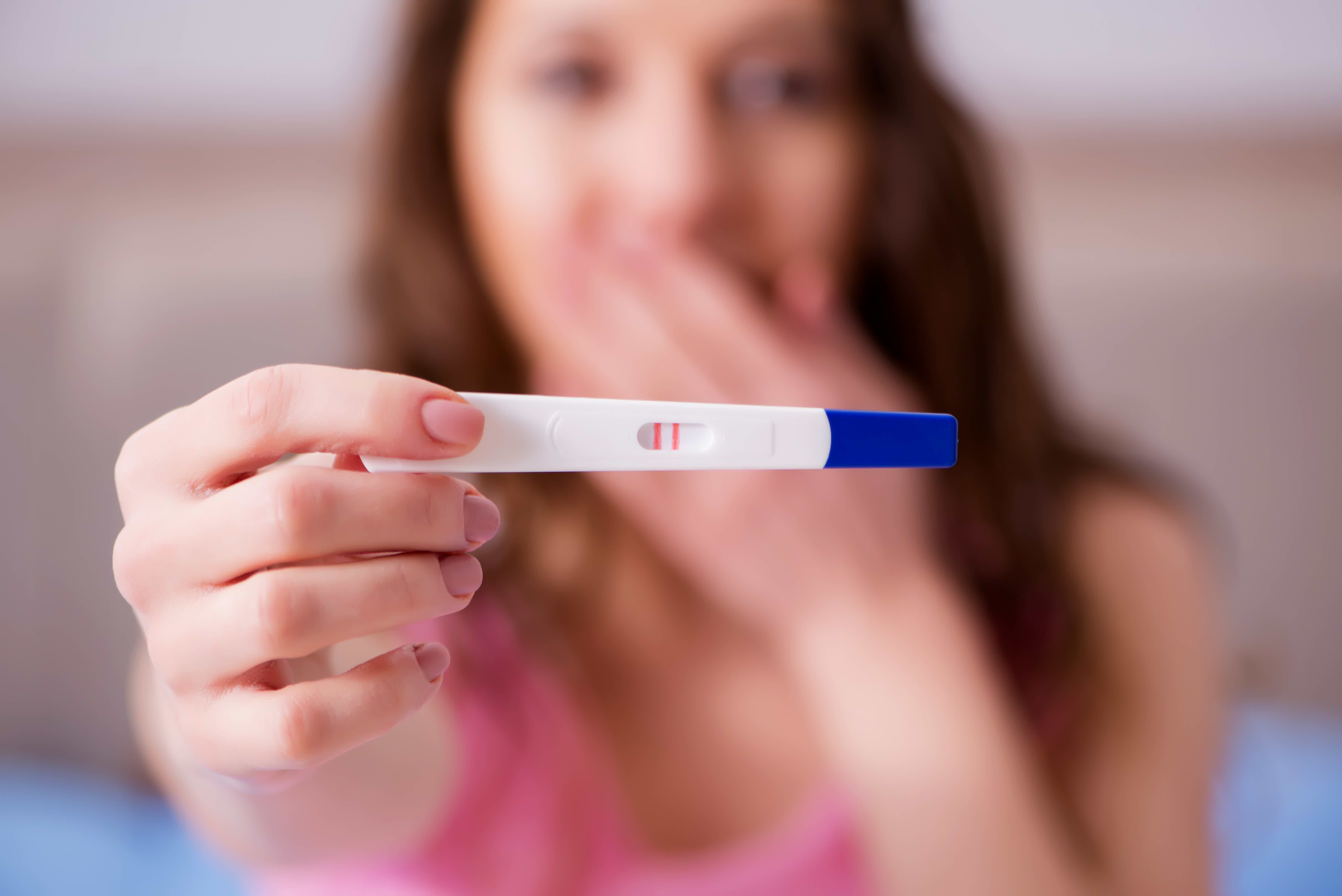 Mulher surpresa apontando teste de gravidez para câmera