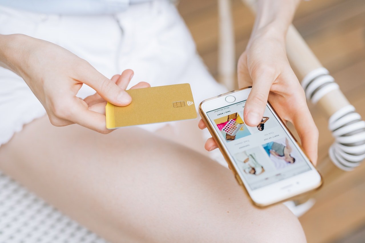 Mulher segurando cartão de crédito dourado ao lado do seu celular.