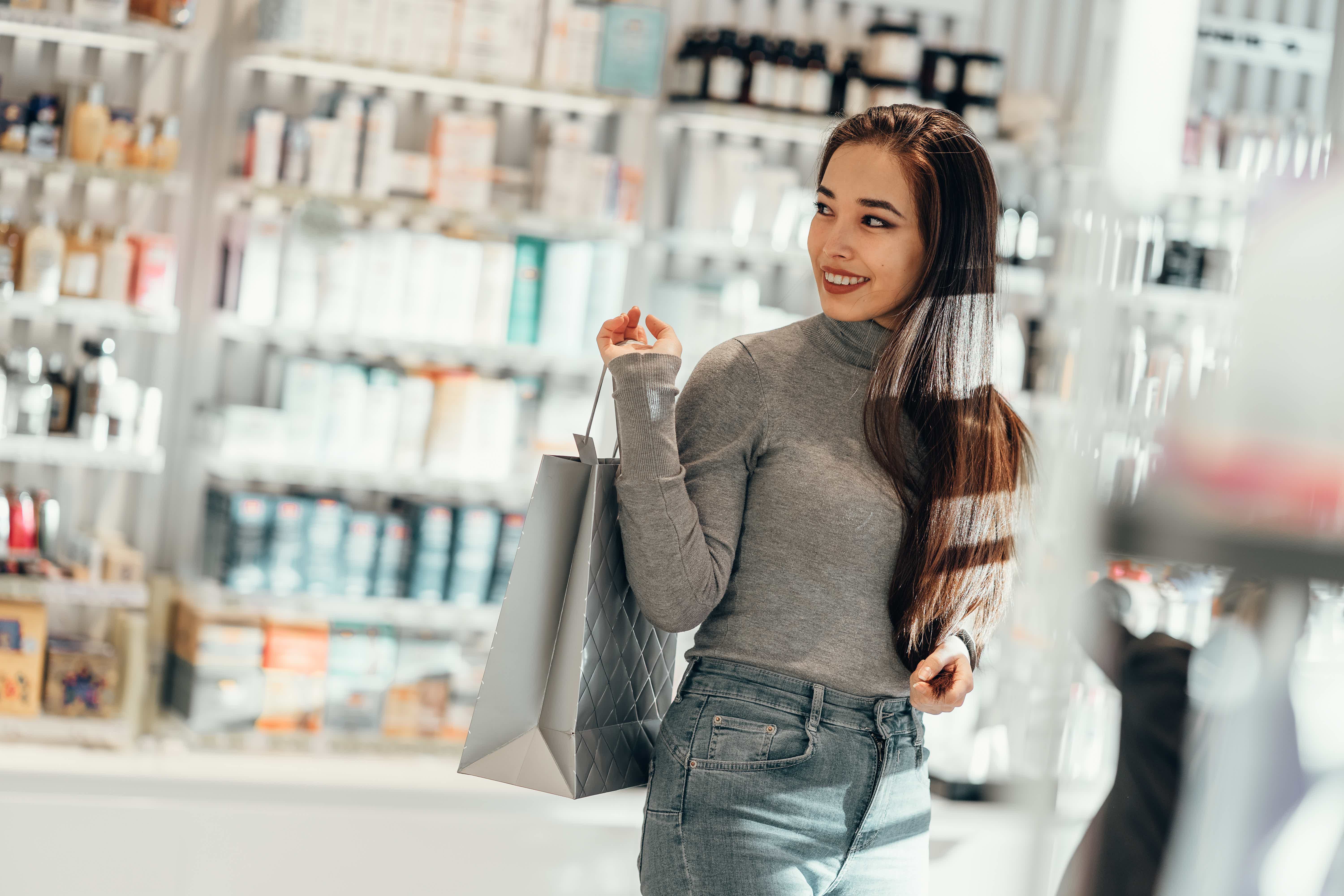 Mulher saindo de loja de cosméticos com sacola e sorrindo