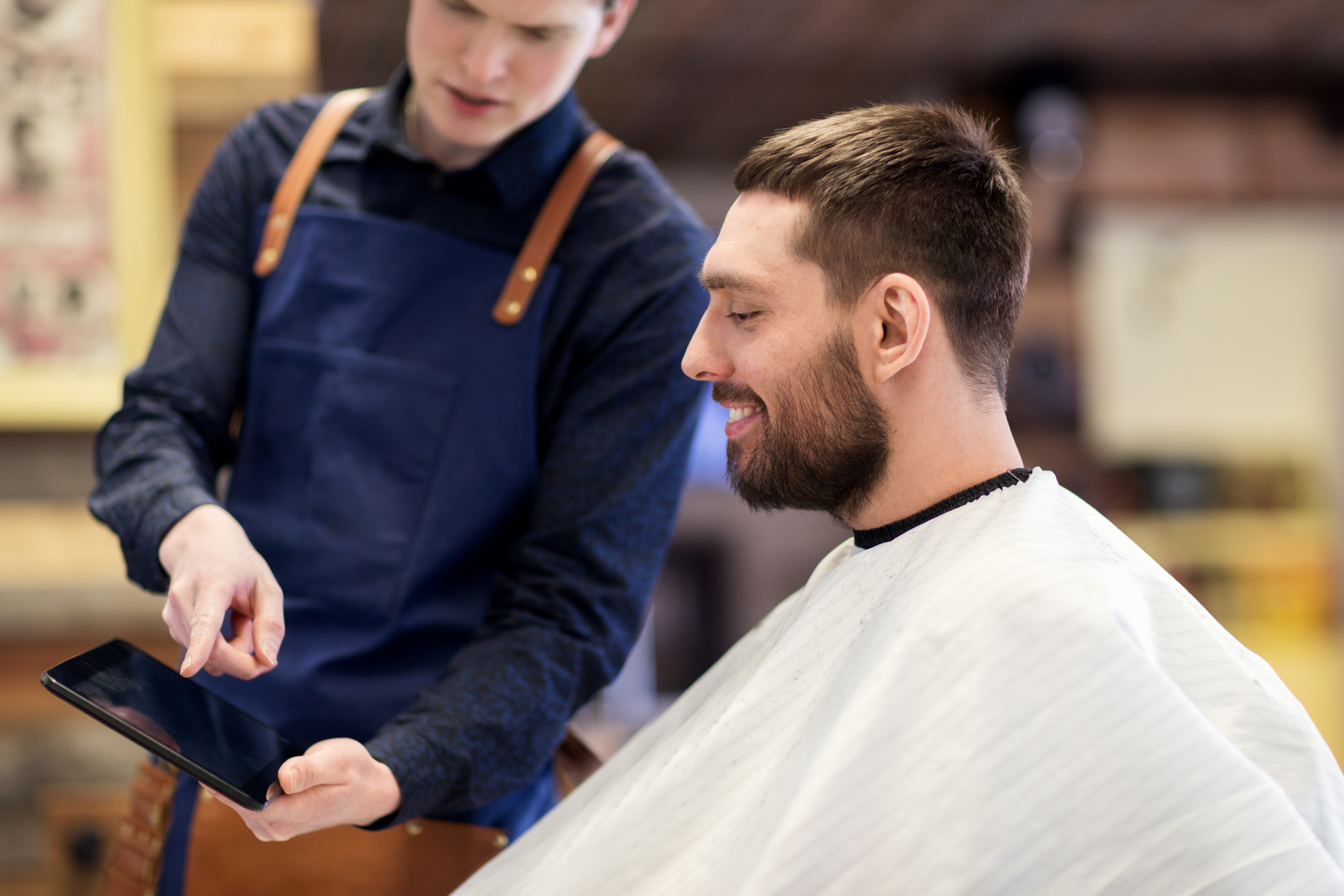 Homem sentado em barbearia olhando tablet